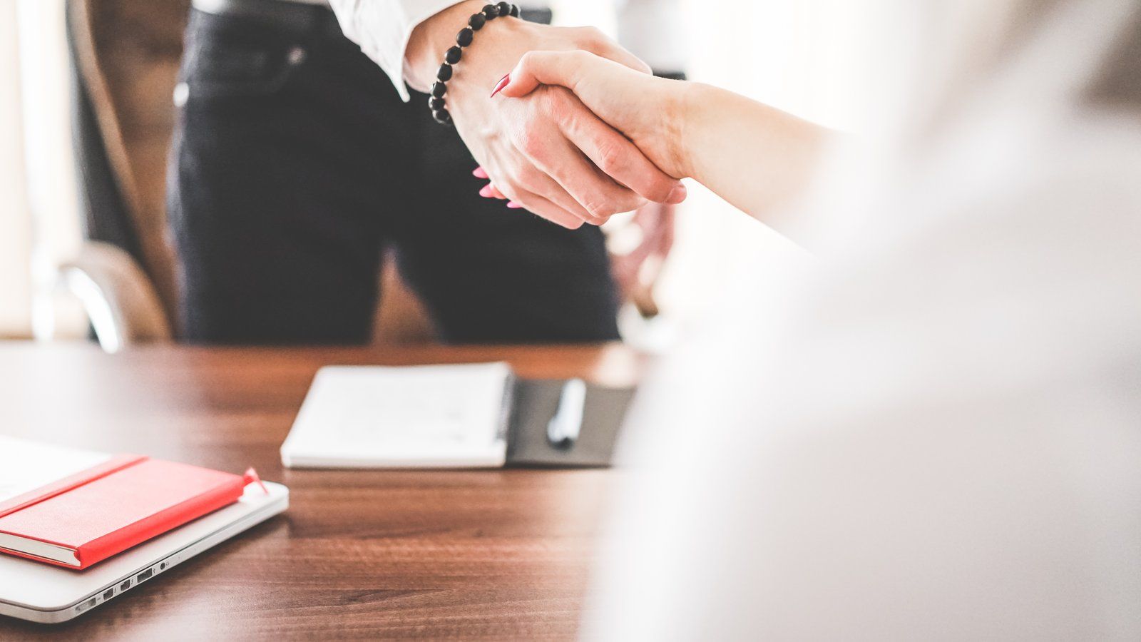 Two people shaking hands over an office desk after a hiring decision