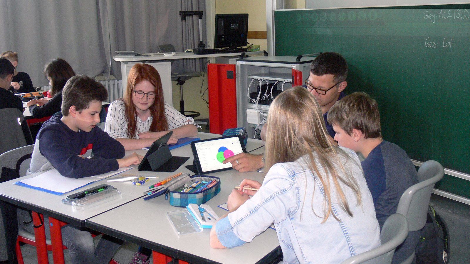Pupils and a teacher working on tablets around a classroom table
